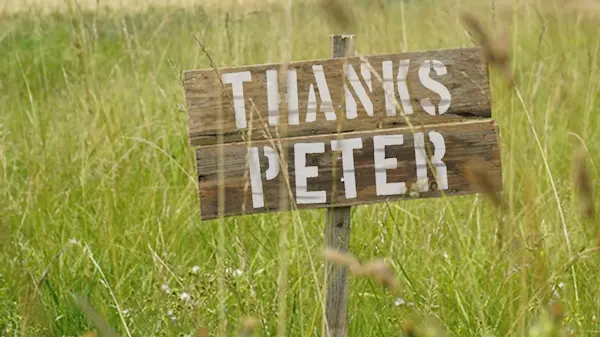 A hand-painted wooden sign in long grass reading “Thanks Peter”